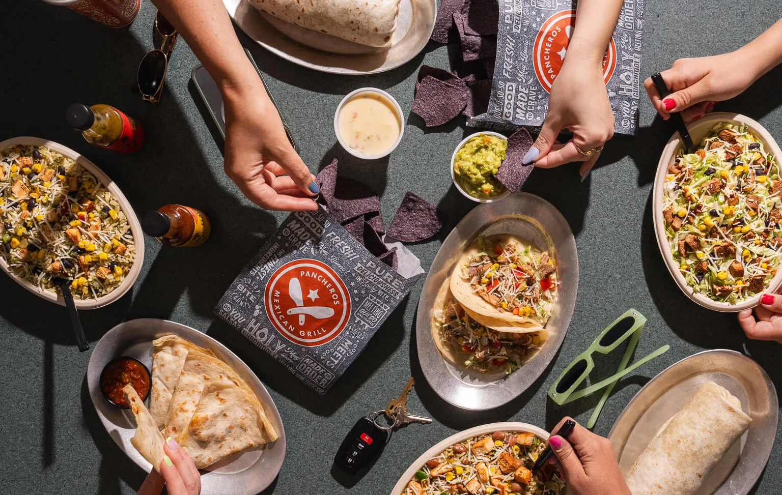 Burritos, tortila chips and queso, bowls, and quesadillas with many hands digging in