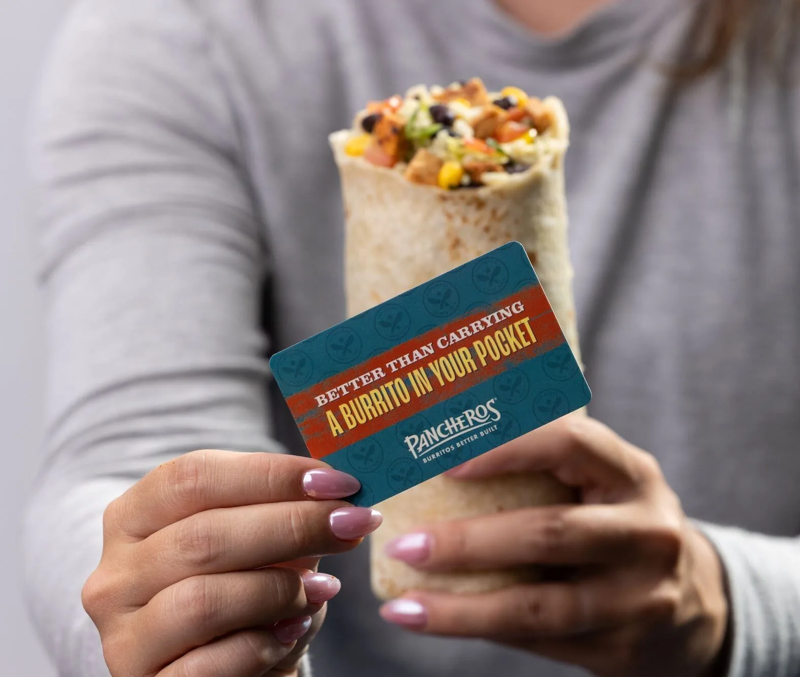 Holding a Pancheros gift card in one hand and a burrito in the other