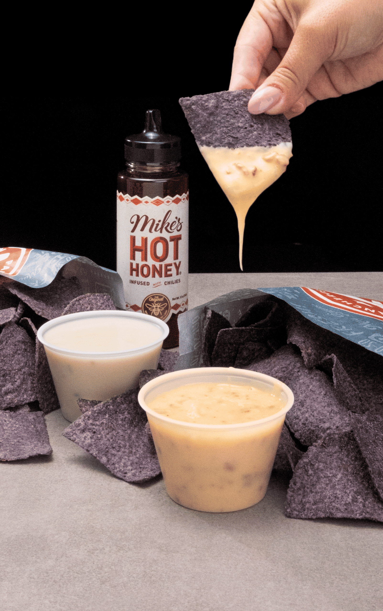 Pancheros' Mike's Hot Honey Bacon Queso and signature queso being dipped with a blue corn tortilla chip
